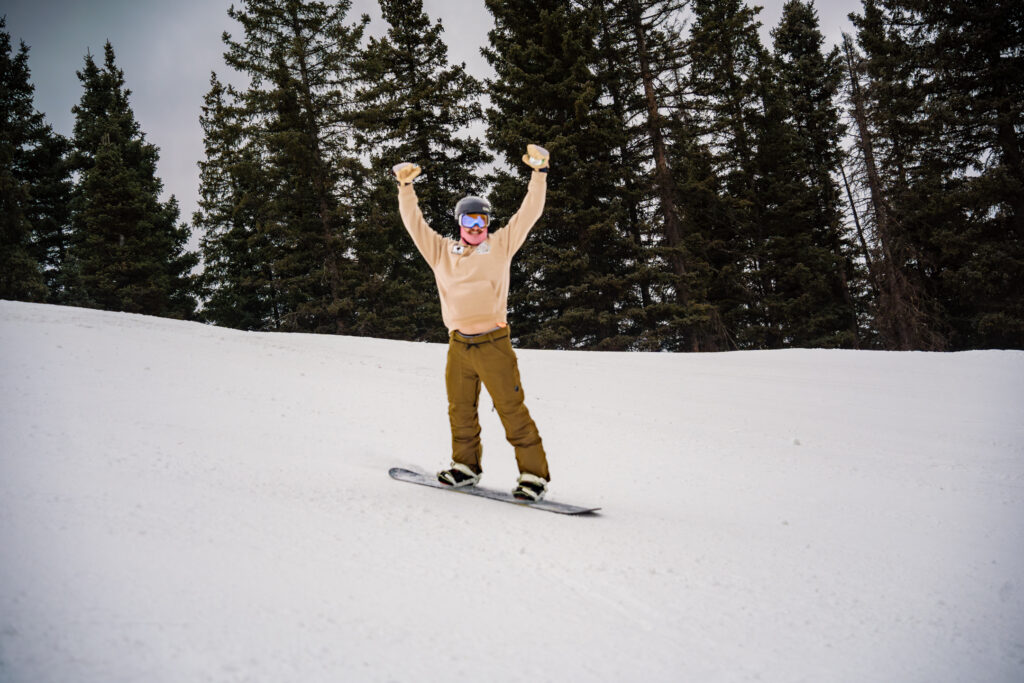 A snowboarder lifts arms in a cheer on opening day