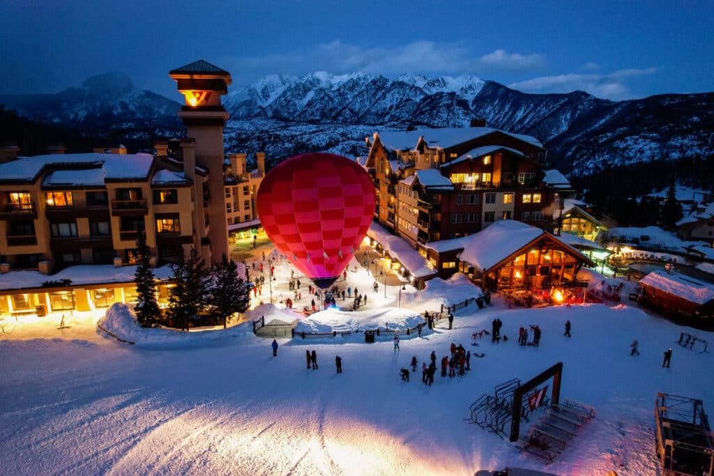 A hot air balloon glows in the base area at a ski resort