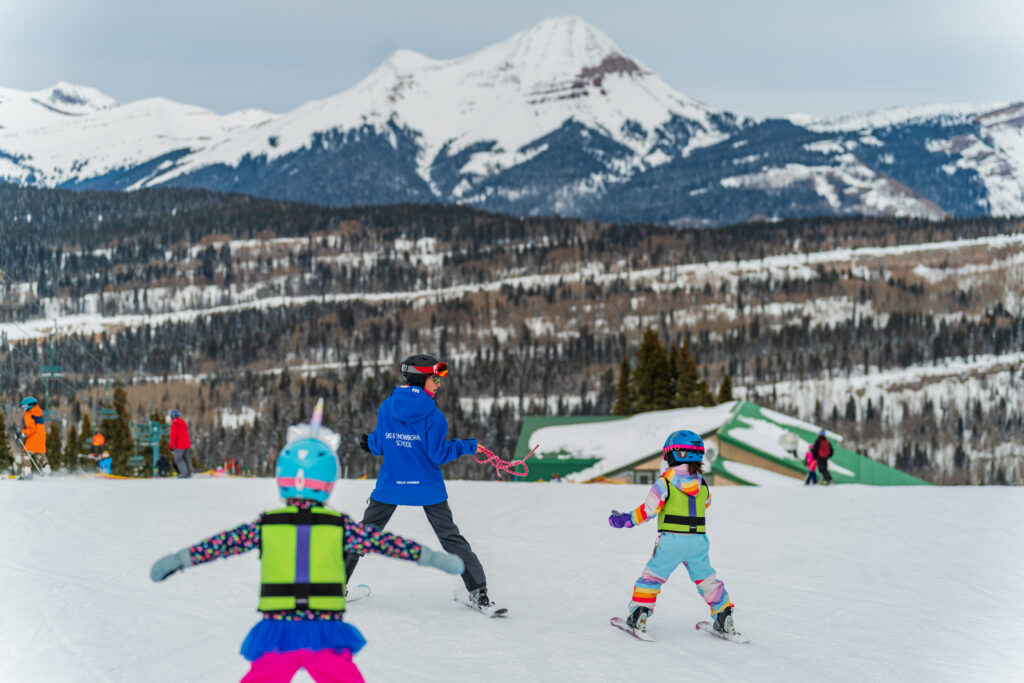 Young kids follow ski instructors pizza turns with Engineer Mountain in the background