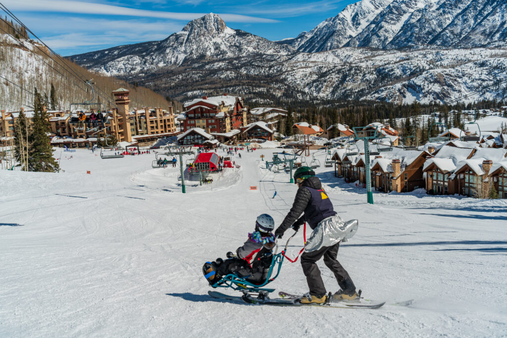Adaptive Sports instructor guides a mono sit ski down to the base area of Purgatory Resort