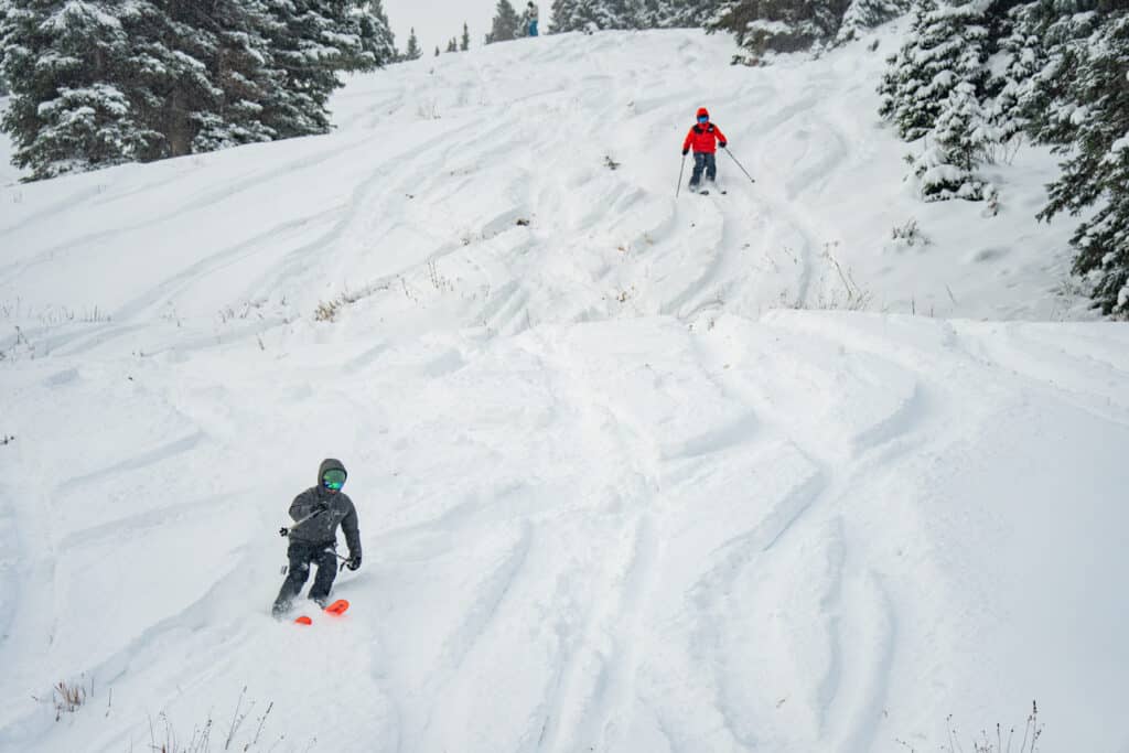 Two skiers descending a slope with fresh snow on it