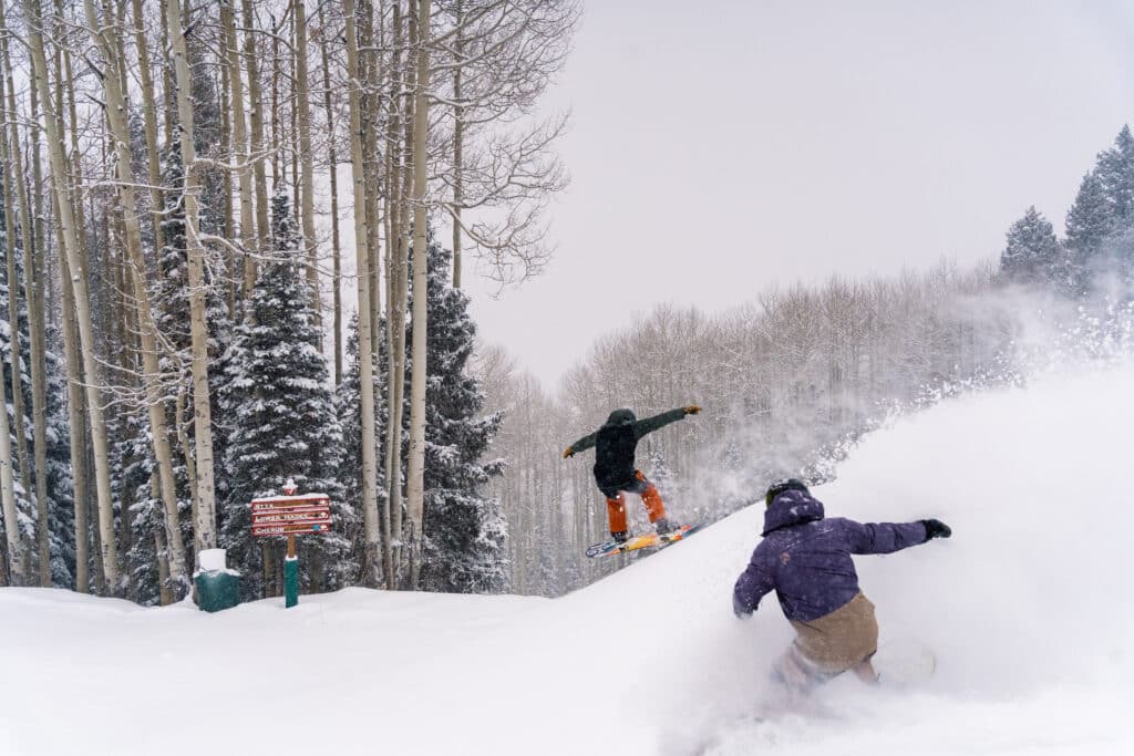 Snowboarder slashes snow while other rider catches air