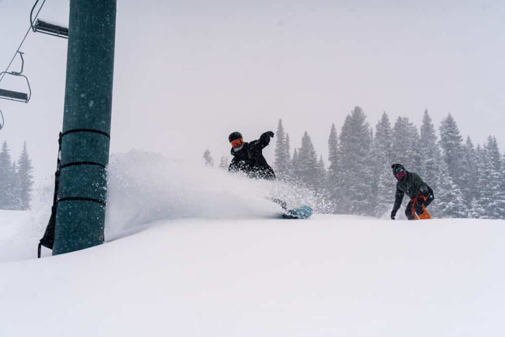 Snowboarders glide over fresh powder beneath a ski lift