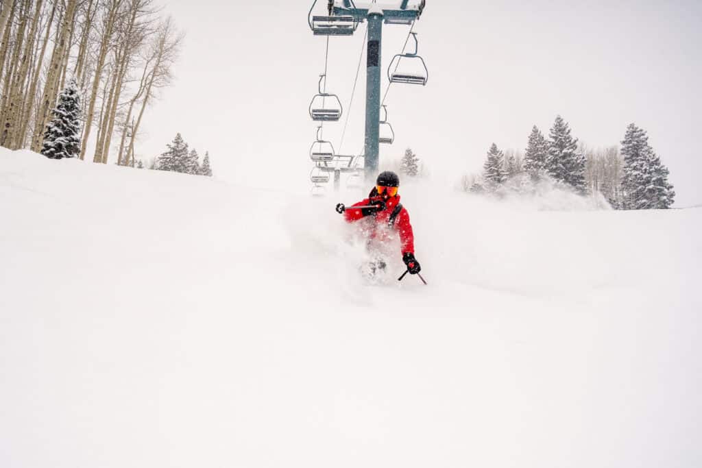 A skier in red rides through powder under a ski lift