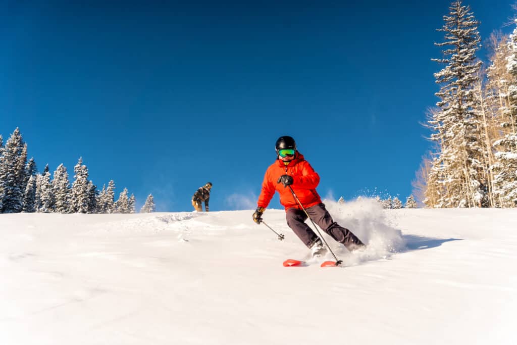 Skier wearing a red jacket takes a turn in some fresh snow on a bluebird day