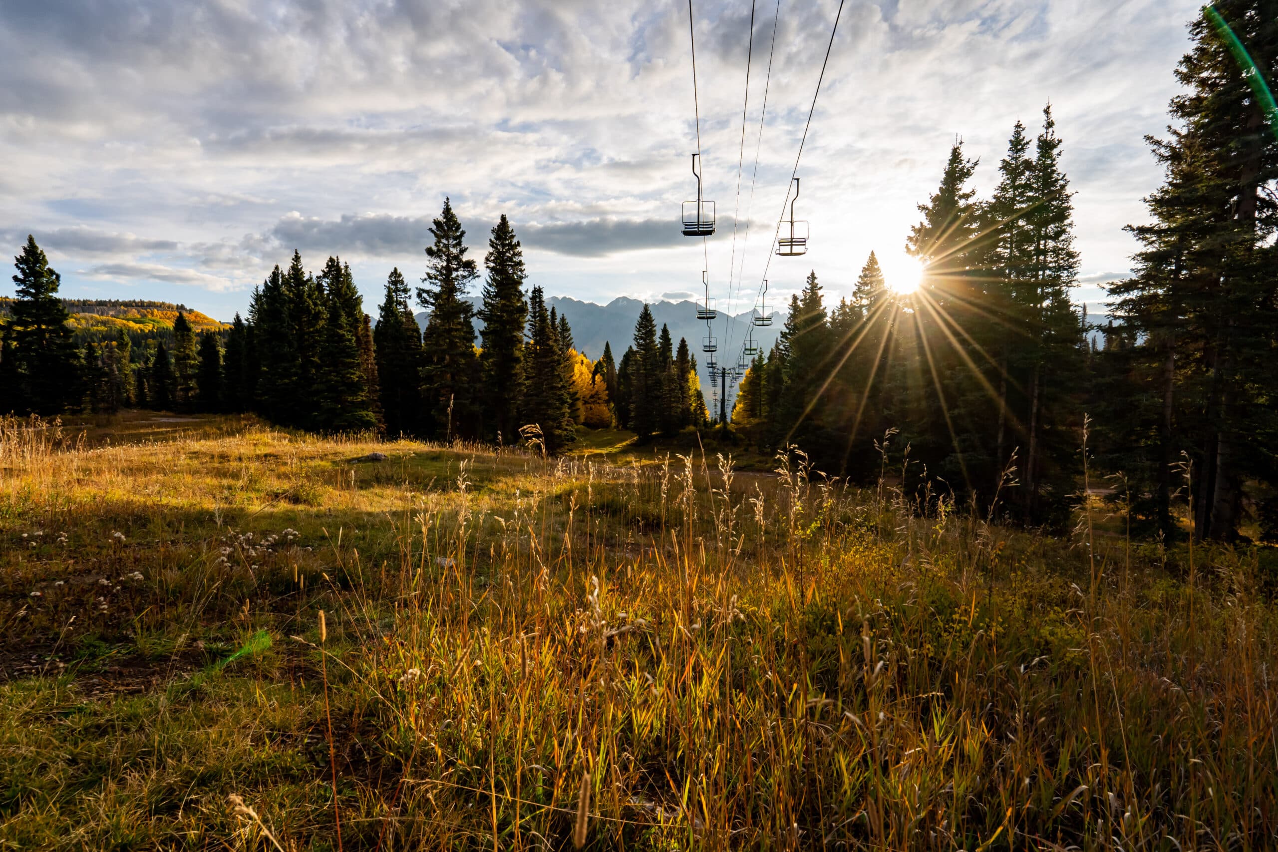 Late summer sun on mountain side grass with a ski lift silhouetted against the sky.
