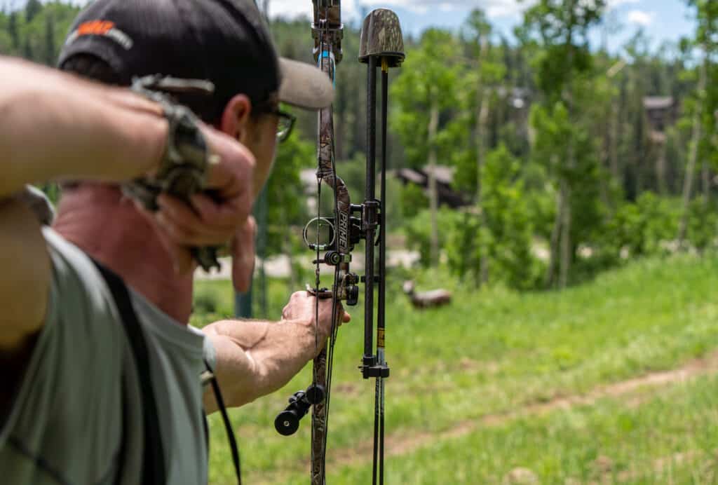 A man aims his bow at a target in the distance