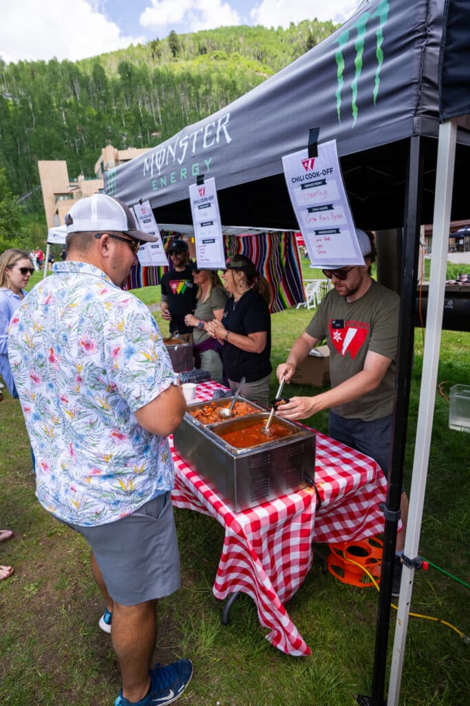 a man in a Purgatory resort t-shirt serves chili to a guest outside on the Purgatory beach