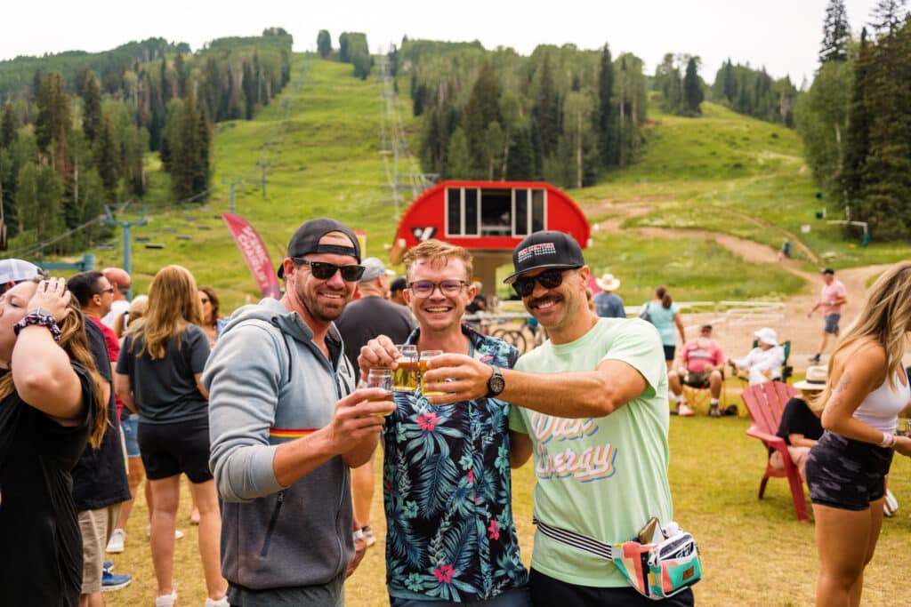 Men Cheers their sample glasses in front of Lift 1 during Summer brew 2024 at Purgatory Resort