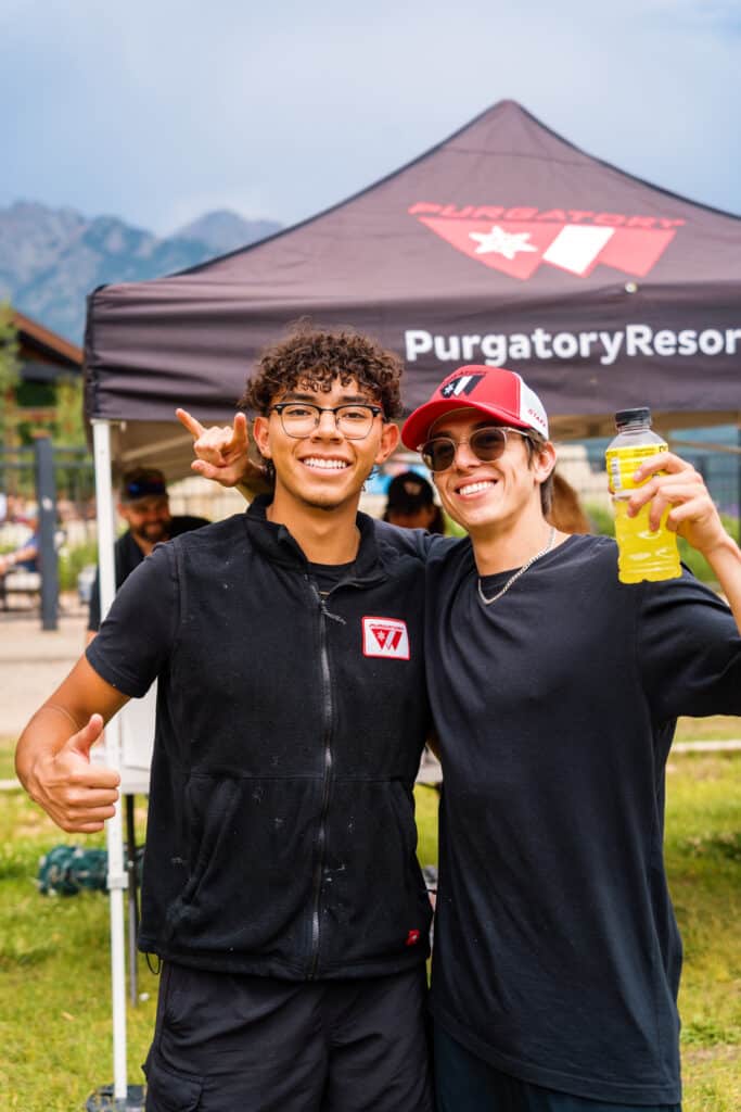 Two men in black shirts smile in front of a Purgatory Resort Tent
