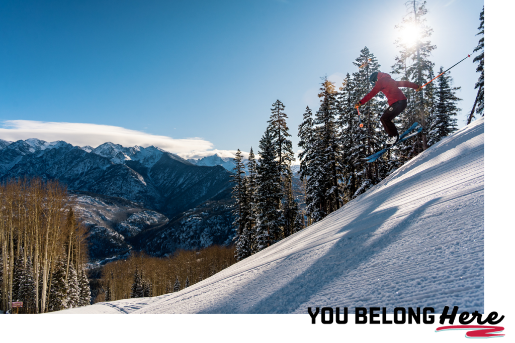 skier in pink jumps majestically. text is you belong here.