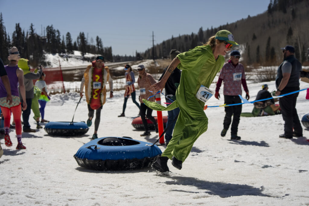 A woman in a dinosaur costume sprints ahead pulling a tube behind her