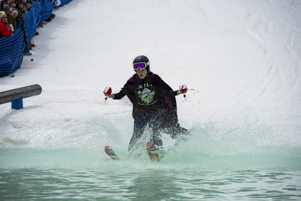 Skier holding two wine glasses skims the pond